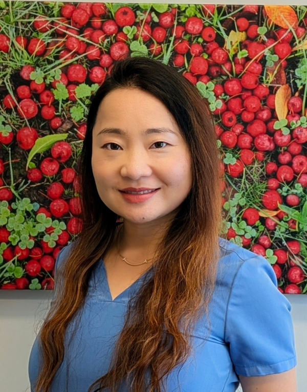 Woman in a blue blouse smiling in front of a red fruit-patterned wall. Cece - Hygienist