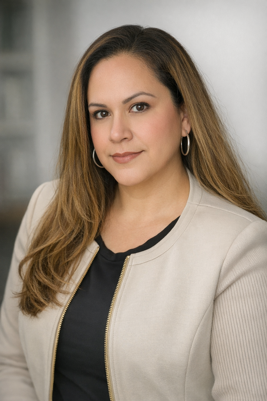 Portrait of a person in a beige jacket against a gray studio background Maria - Office Manager