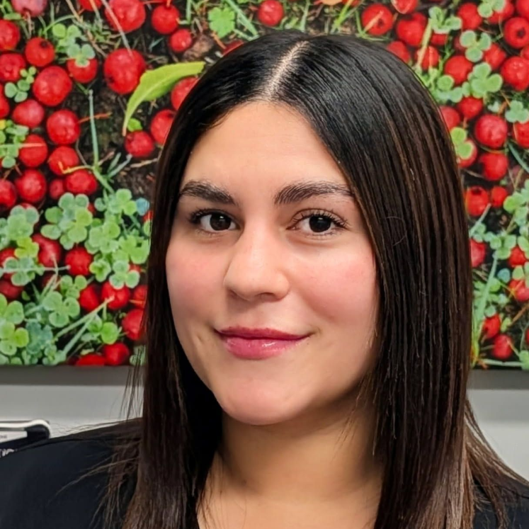 Portrait of a woman with dark hair in front of a red berry wall Monica - Dental Assistant
