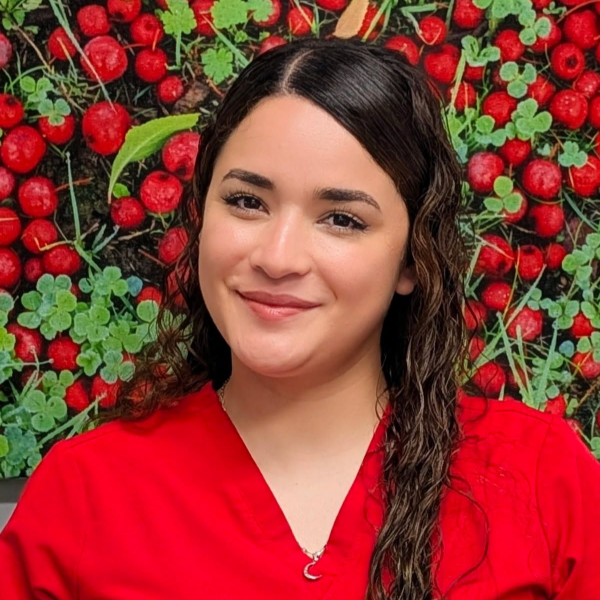 Smiling person in a red blouse in front of a strawberry-covered wall Cece - Hygienist