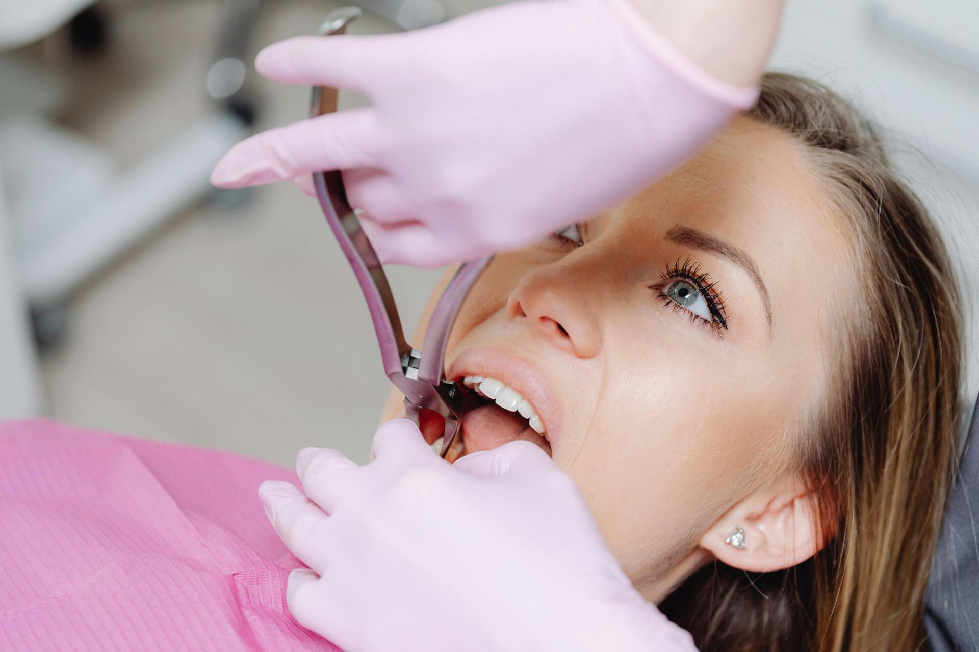 Dentist extracting a tooth from a woman's mouth with forceps in a dental office.