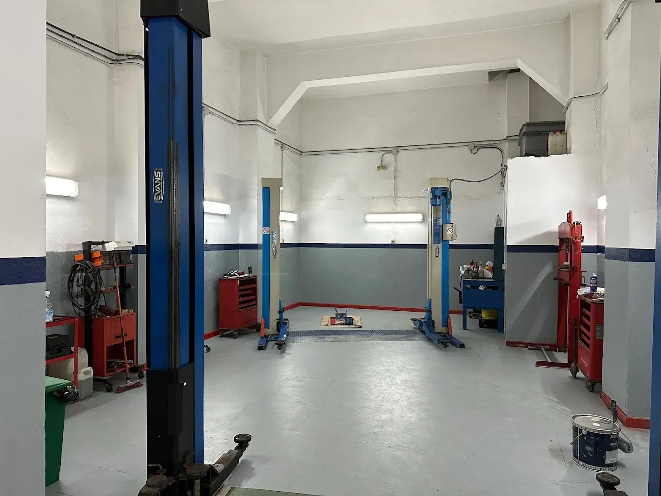 Un taller de reparación de automóviles vacío y bien iluminado, con elevadores de dos postes y herramientas contra las paredes.