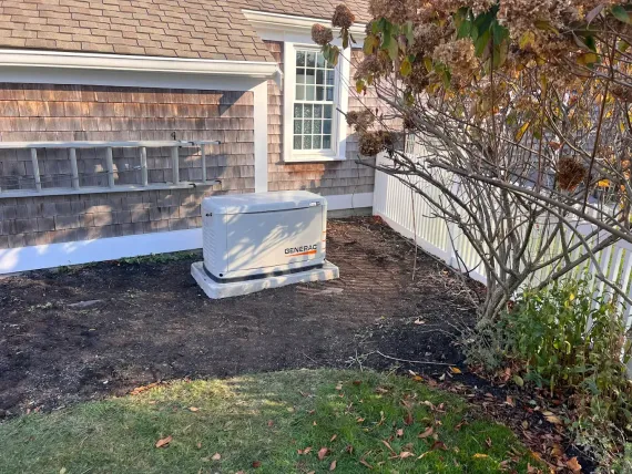 Residential yard with a beige utility box beside a house, a fence, and shrubs.