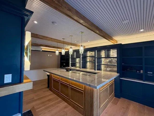 Empty modern kitchen with dark cabinets, central island, pendant lights, and wood-beamed ceiling