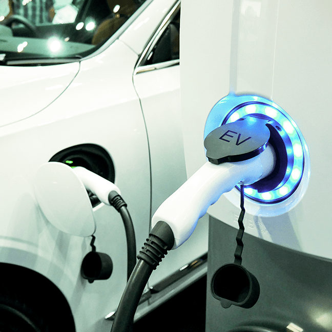 White EV charging at a glowing blue charging port beside another plugged-in car