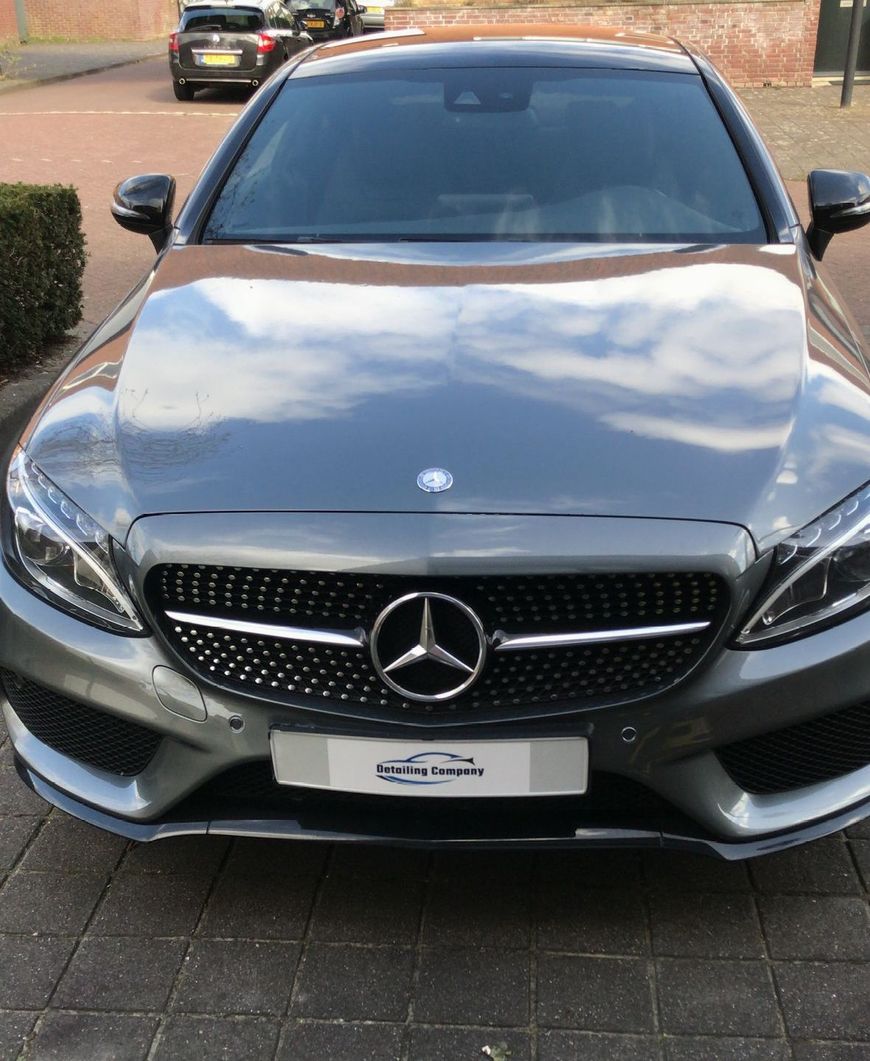 Vooraanzicht van een zilverkleurige Mercedes-Benz geparkeerd op een oprit, met zwarte grille en getinte ramen.