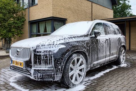 Een SUV, bedekt met dik zeepschuim, staat geparkeerd op een oprit naast een huis.