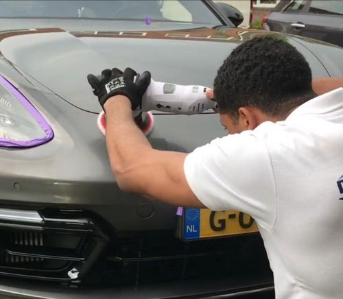 Een persoon brengt beschermfolie aan op de motorkap van een grijze auto in een garage.