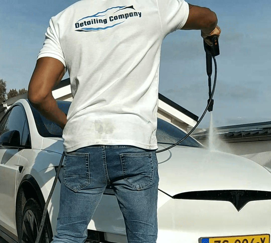 Autodetailer reinigt de voorkant van een witte sportwagen met een hogedrukreiniger in de buitenlucht.
