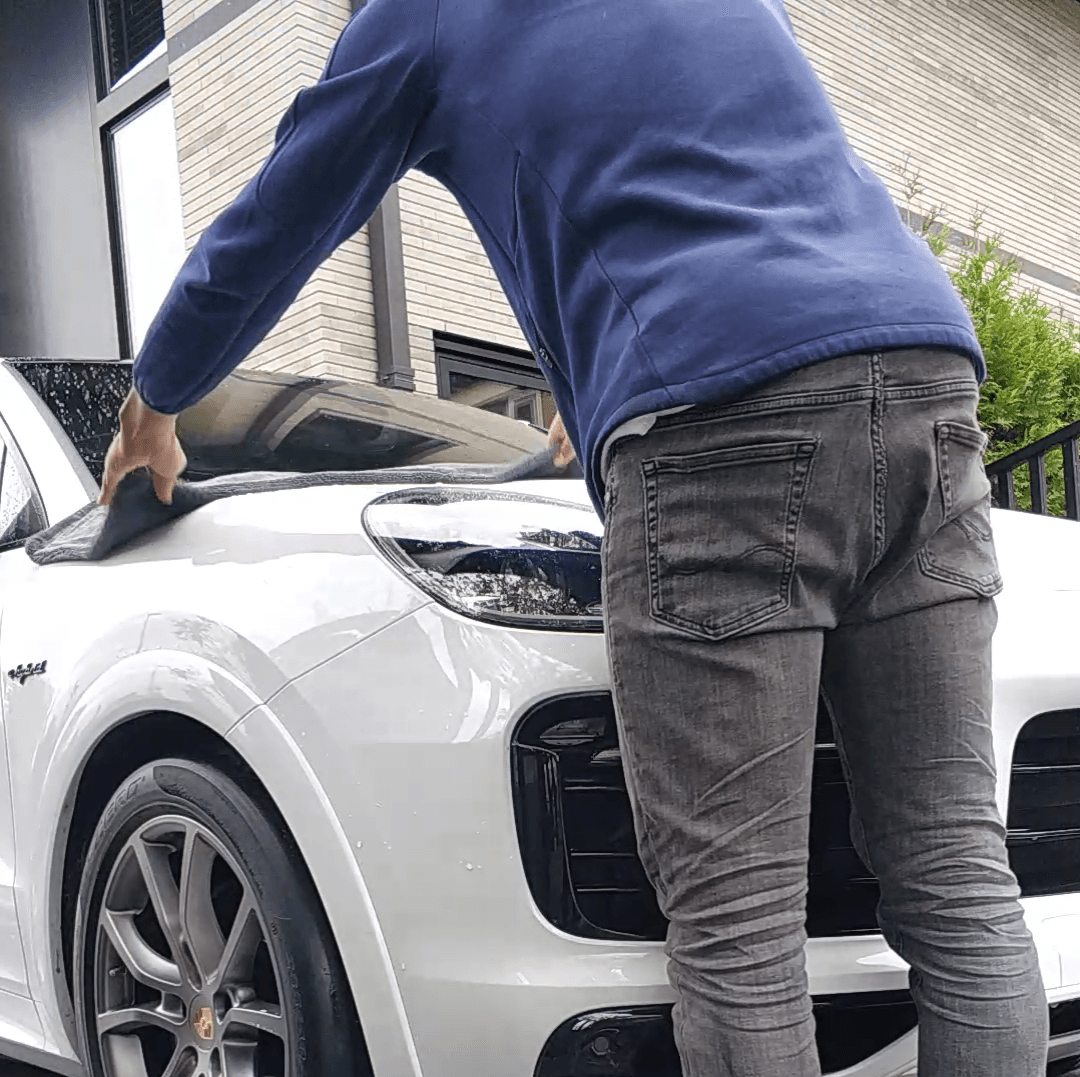 Een persoon maakt de voorruit van een witte SUV schoon op een oprit.