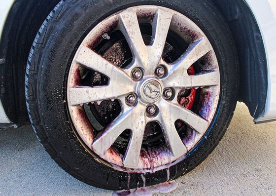 Close-up van een autowiel met een zilverkleurige lichtmetalen velg en een natte band op een lichte ondergrond.
