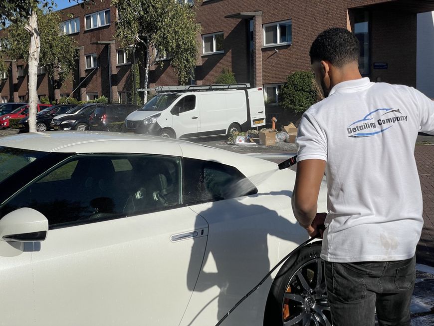 Persoon naast een witte auto voor een bakstenen gebouw, met een rolstoelwiel in de hand.