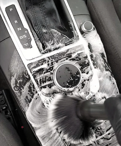 De middenconsole van de auto wordt schoongemaakt met een borstel en zeepschuim rond de versnellingspook.
