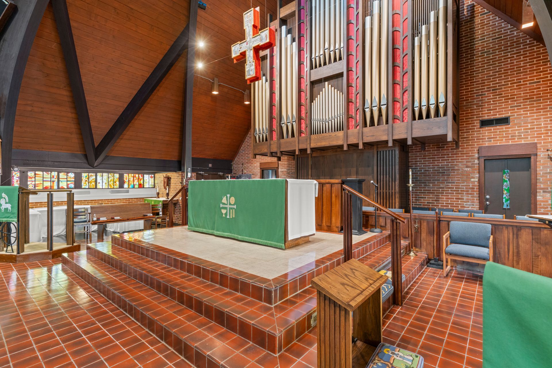 Church sanctuary with brick walls, wooden pews, altar, and large organ pipes under a cross.