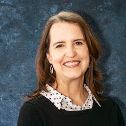 Portrait of a smiling woman in a black sweater against a blue studio backdrop
