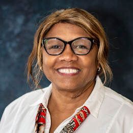 Smiling person wearing glasses and a white blouse with a red patterned collar against a dark backdrop