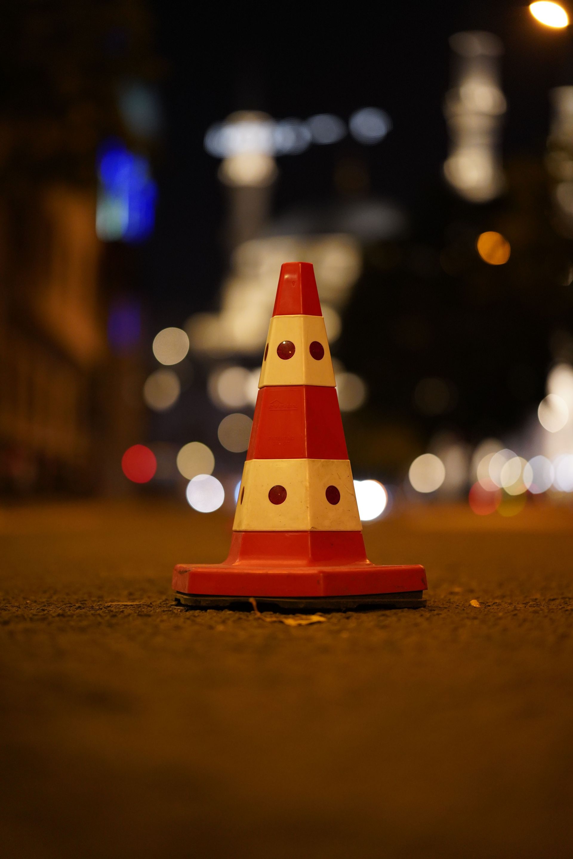 Orange traffic cone on a nighttime street with blurred city lights in the background