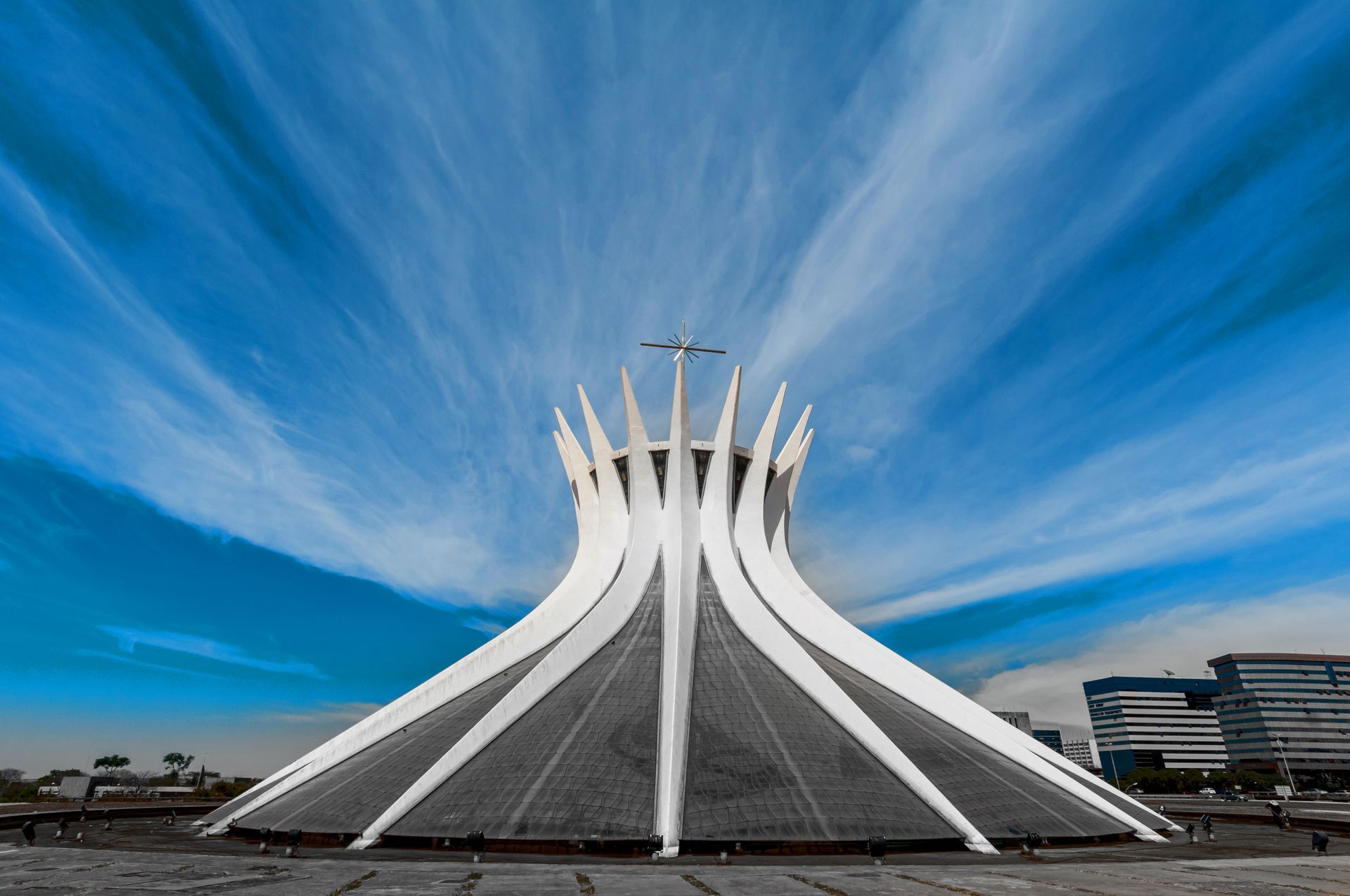 A Catedral de Brasília, uma estrutura branca e hiperbólica com imponentes pilares de concreto, destaca-se contra um céu azul brilhante.
