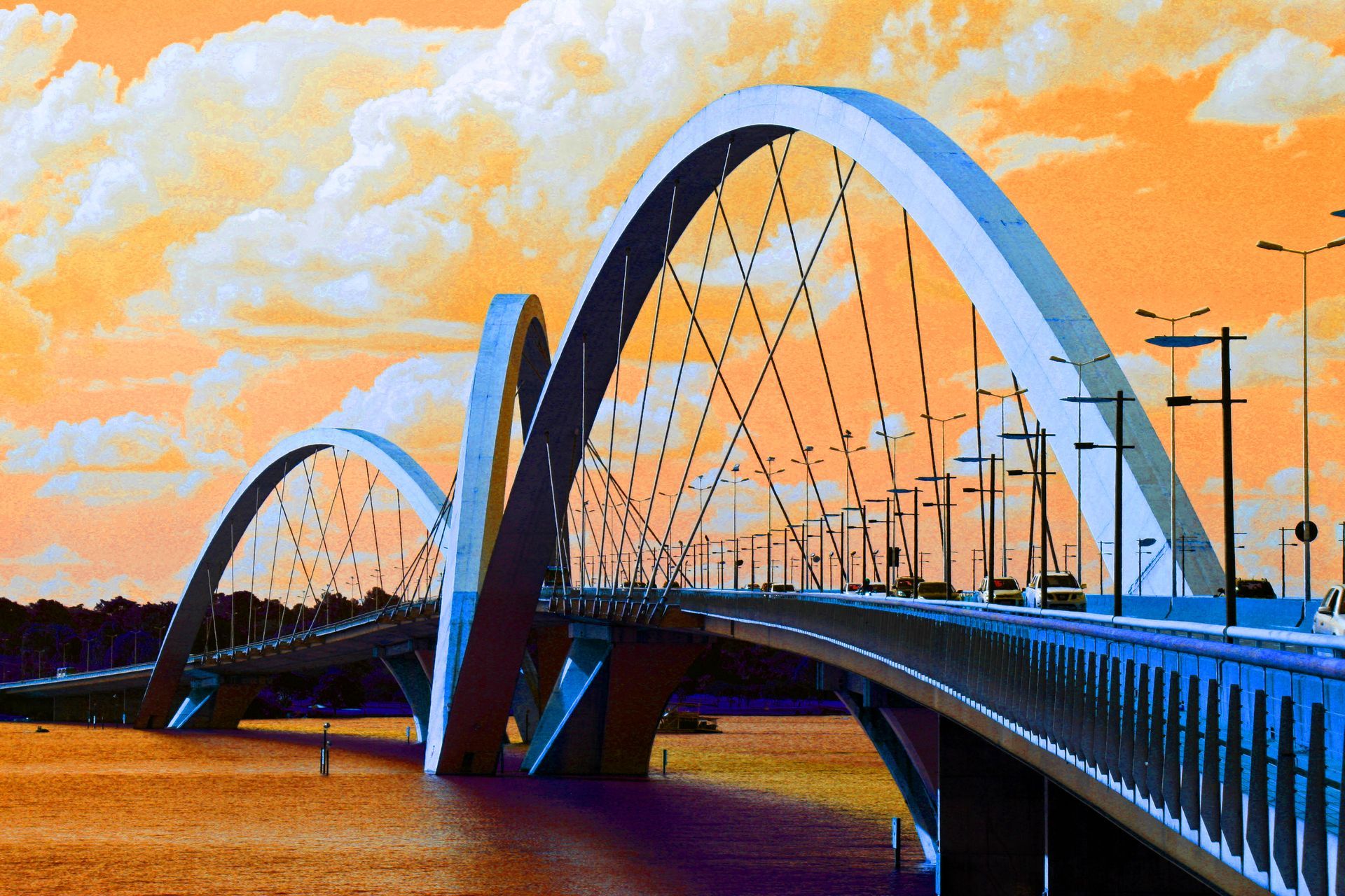A Ponte Juscelino Kubitschek em Brasília, Brasil, apresenta três arcos brancos assimétricos sobre águas de tonalidade alaranjada.