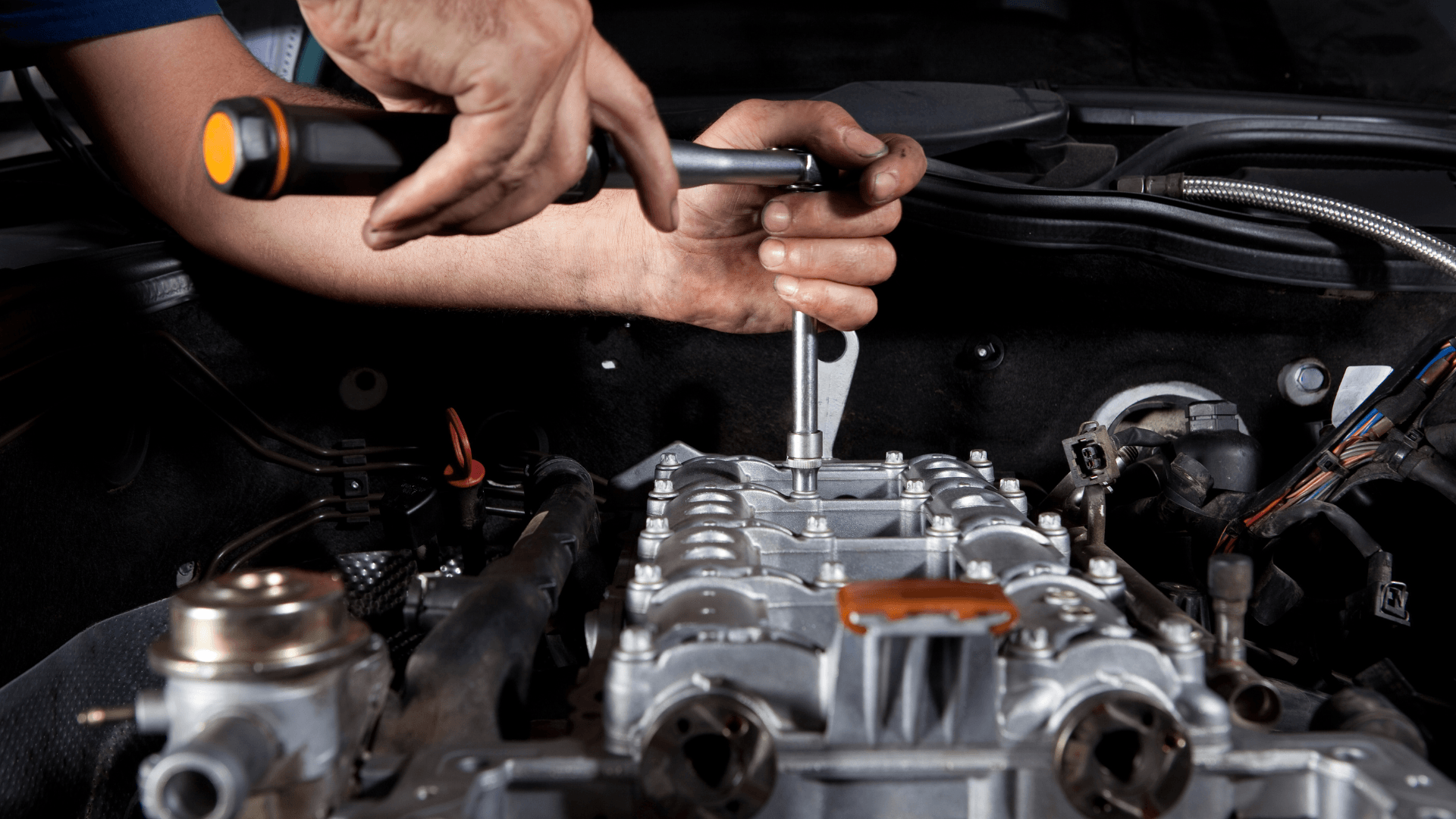 A man is working on a car engine with a wrench.