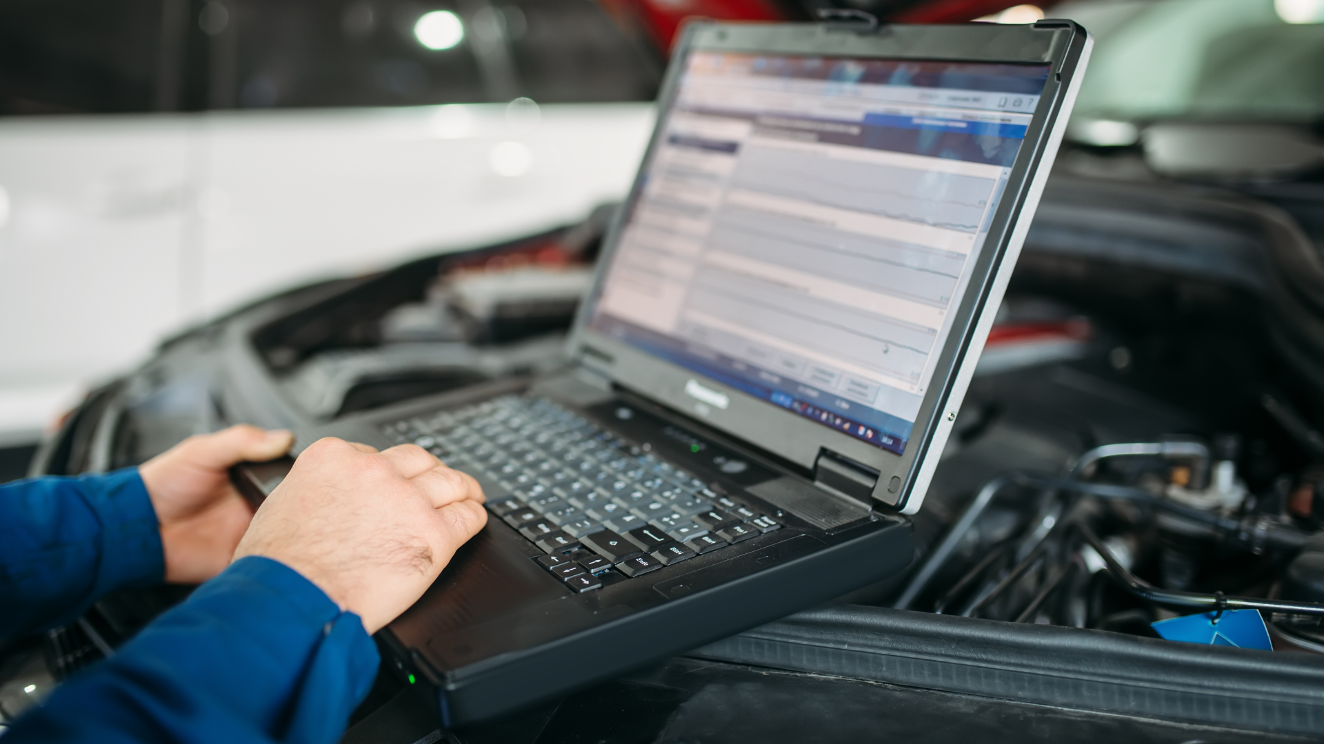 A man is using a laptop computer to check the engine of a car.