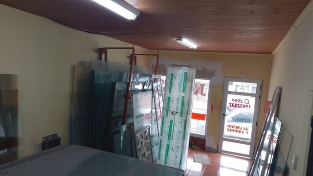 Interior de una pequeña tienda con puertas de cristal, estanterías apiladas y luces fluorescentes.