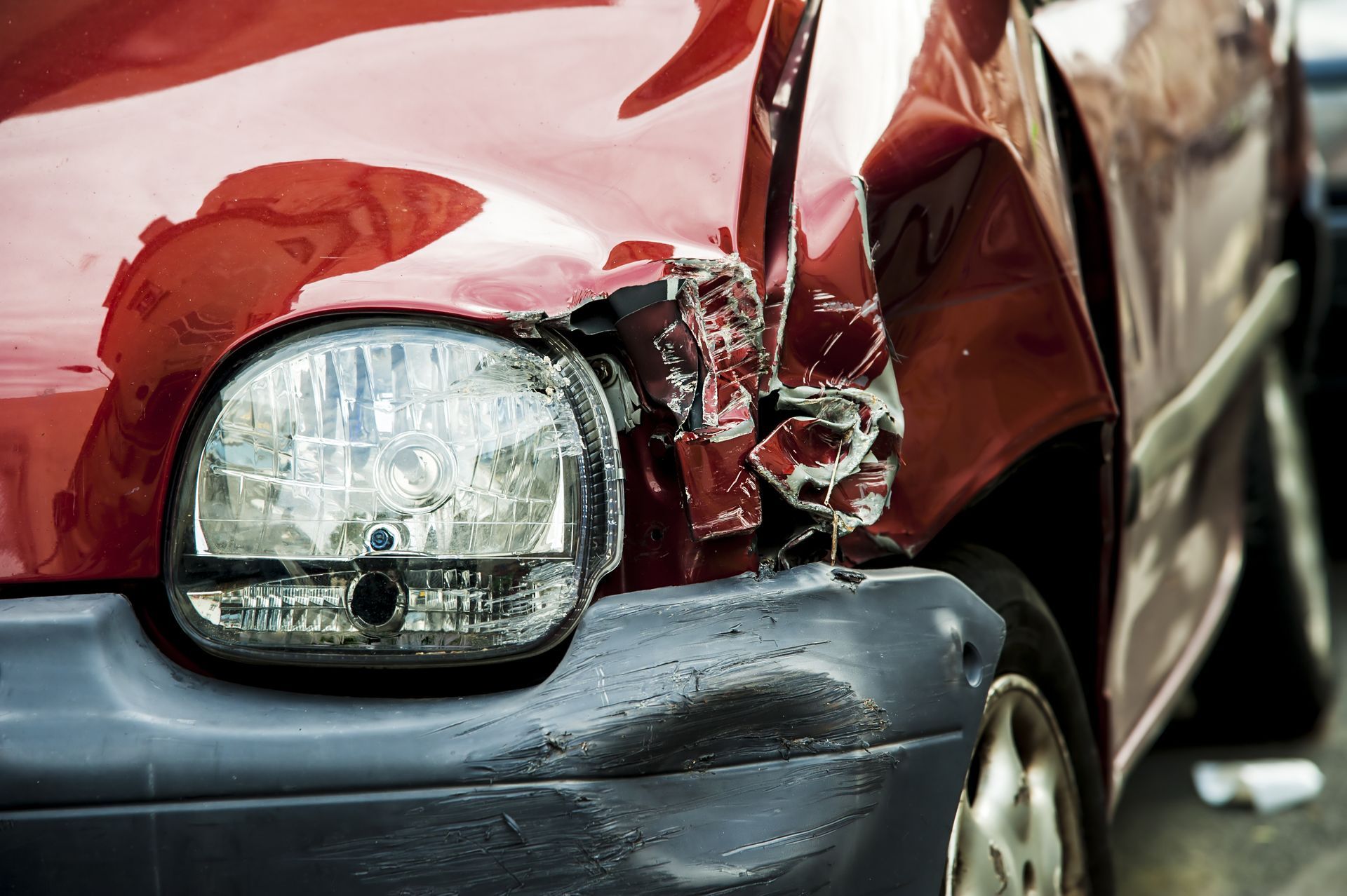 Damaged red car with crumpled front end and broken headlight after a collision