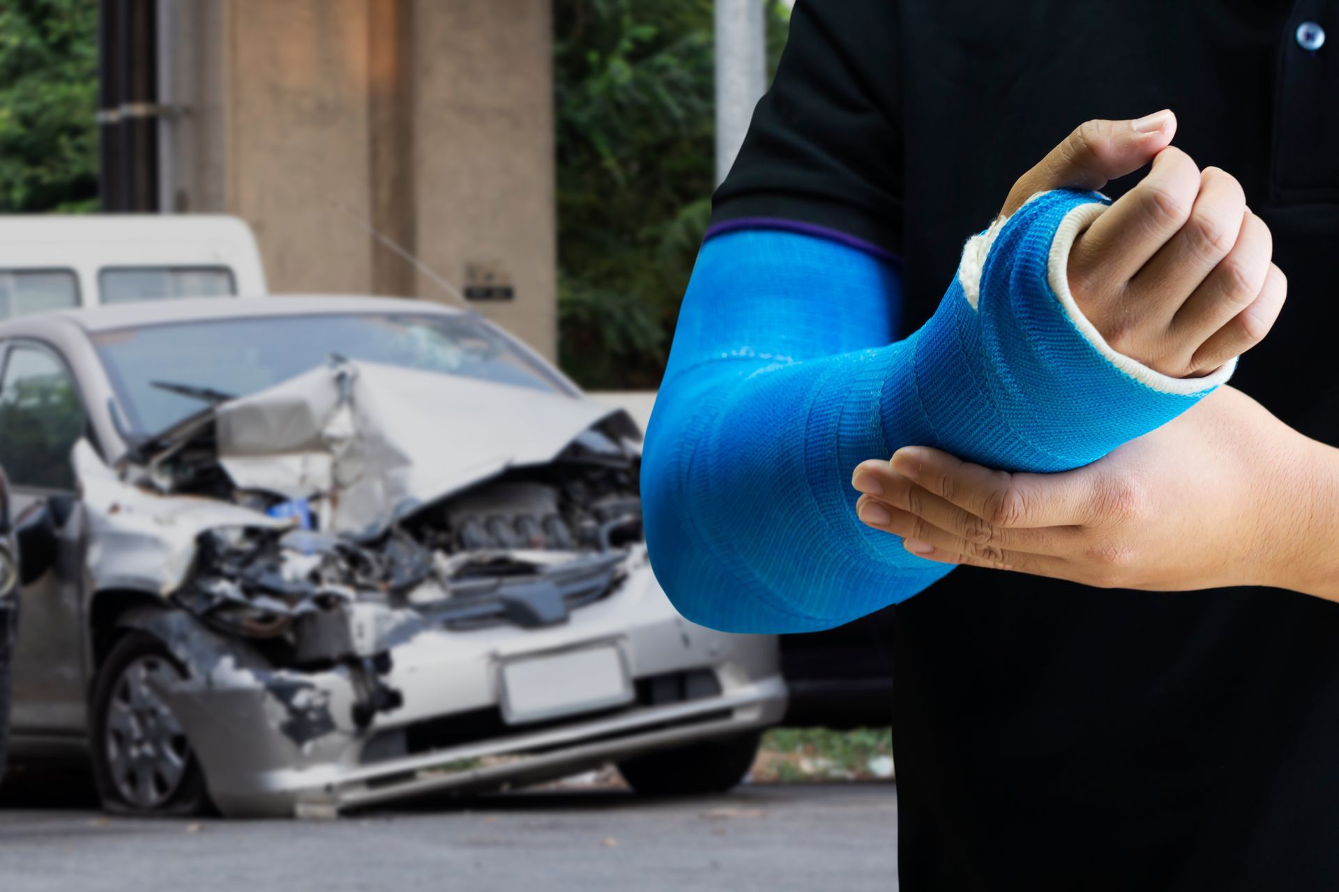 Person with a blue cast on their arm in front of a badly damaged car after a crash