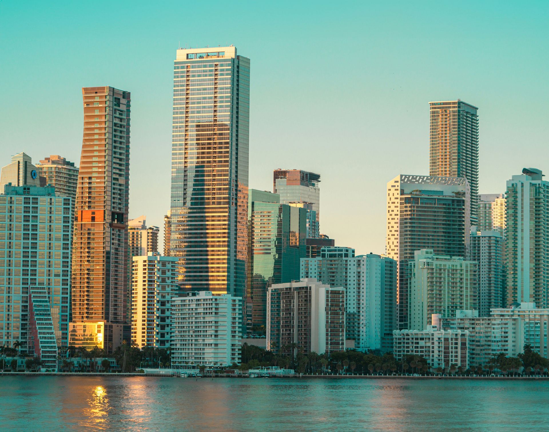 Skyline of Miami skyscrapers reflecting in the water, golden sunlight.