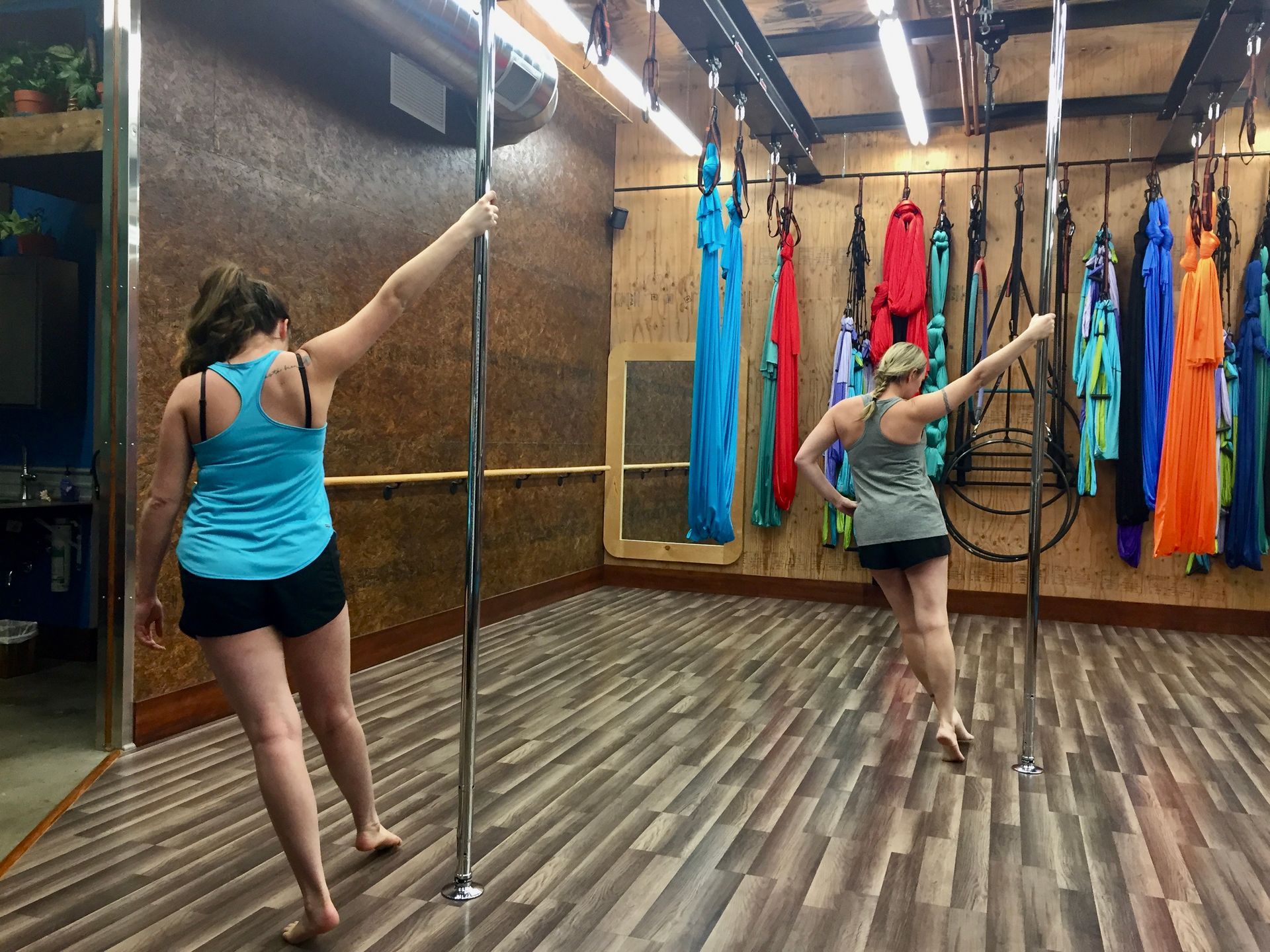 Two people practice aerial dance with silk hammocks in a studio with wooden floors and colorful fabrics.