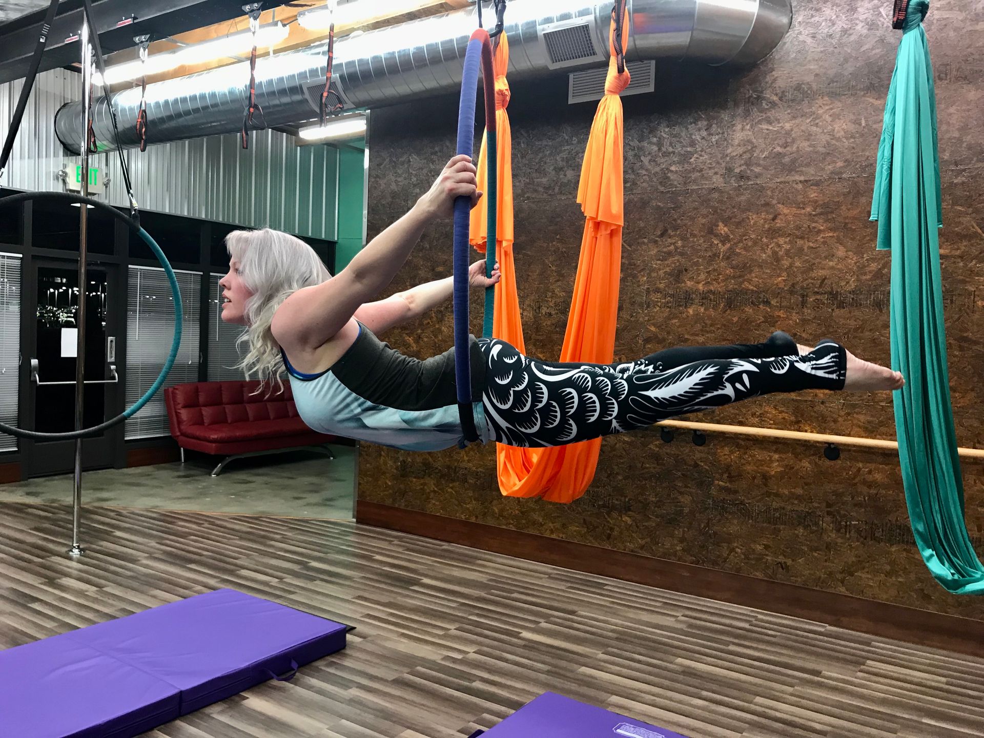 Woman suspended in a yoga sling, holding a horizontal pose in a studio with colorful hammocks.