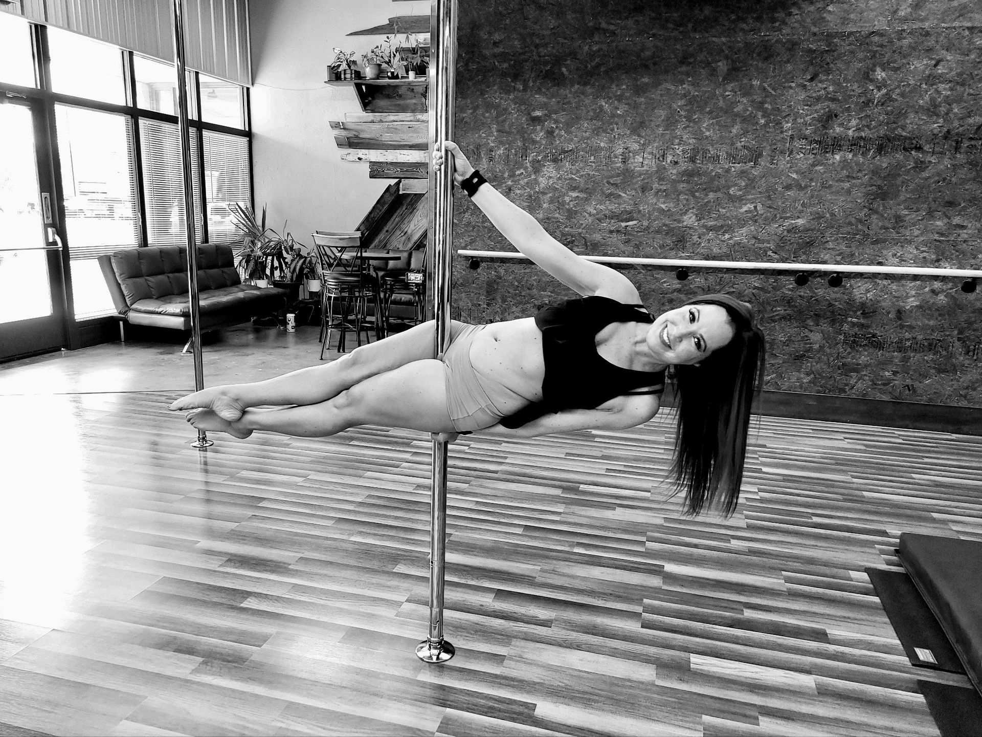 Woman performing a horizontal pole dance hold in a studio with mirrored walls and wood flooring