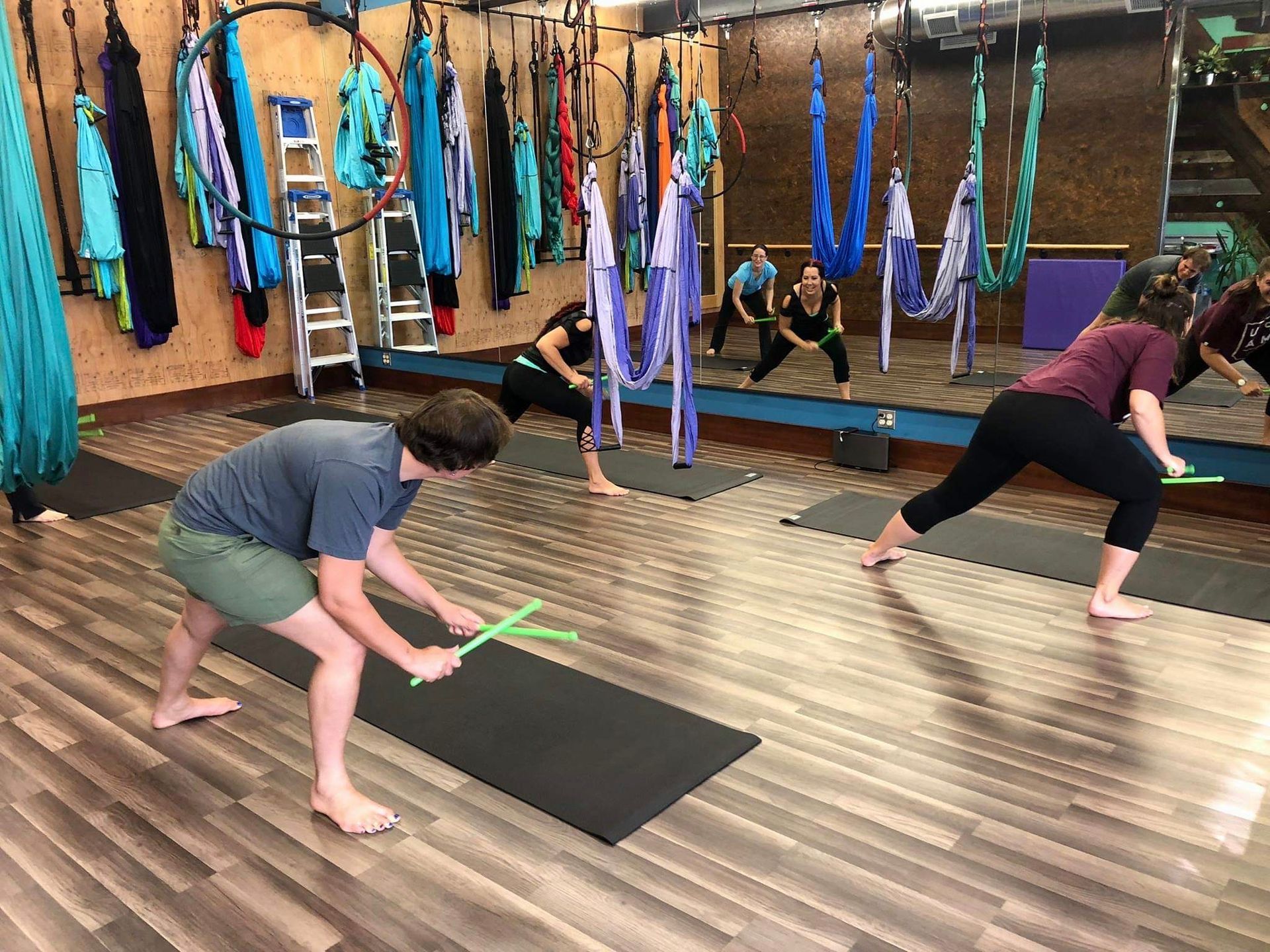 People stretching on mats in a yoga studio with hanging hammocks and wooden floors