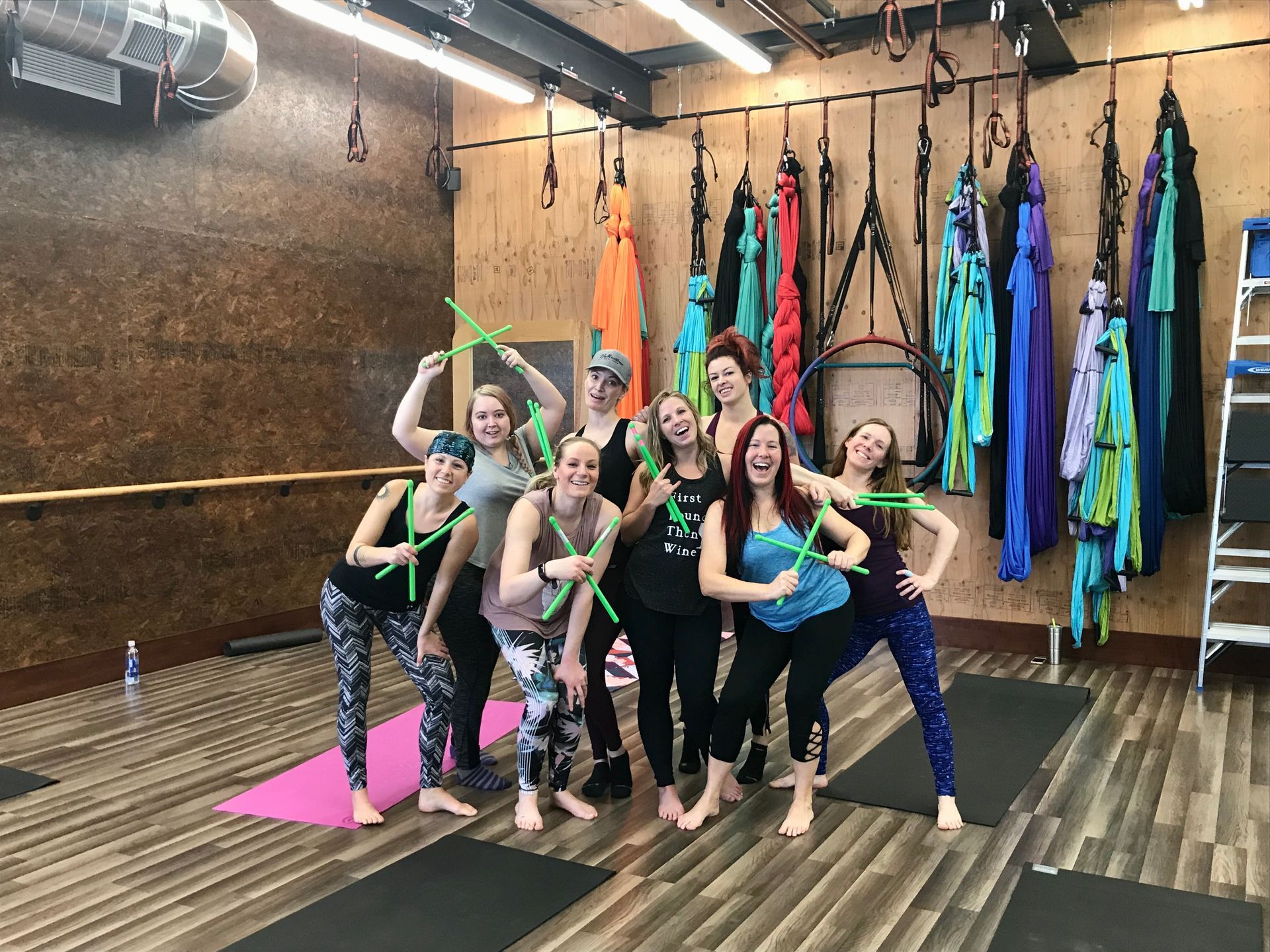 Group posing in yoga studio with colorful aerial silks hanging on the wall