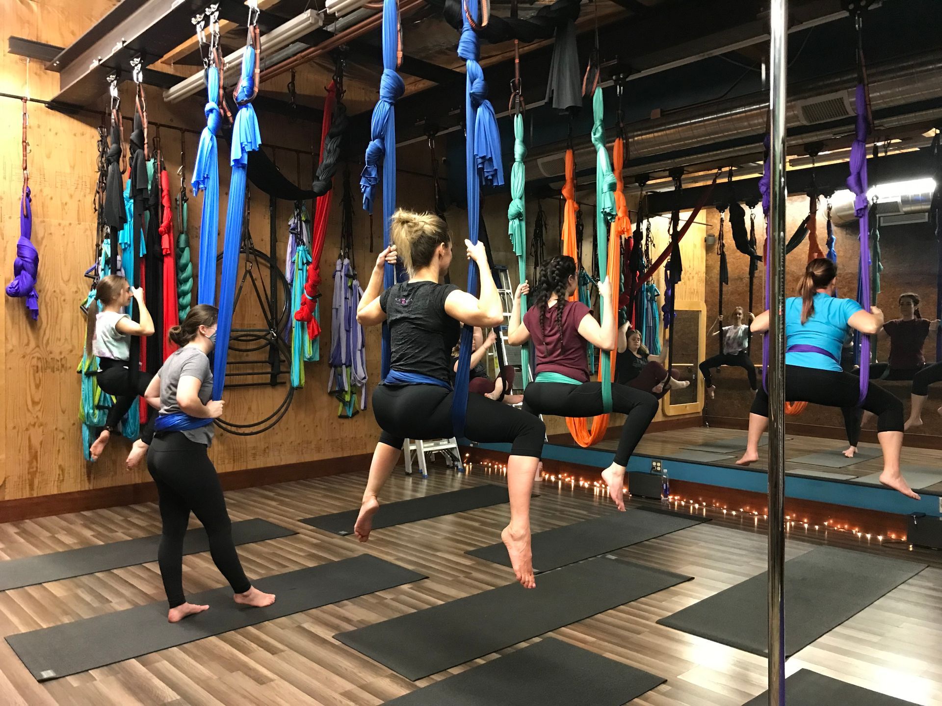 People practicing aerial yoga in a studio, hanging from blue and purple silks over mats and mirrors