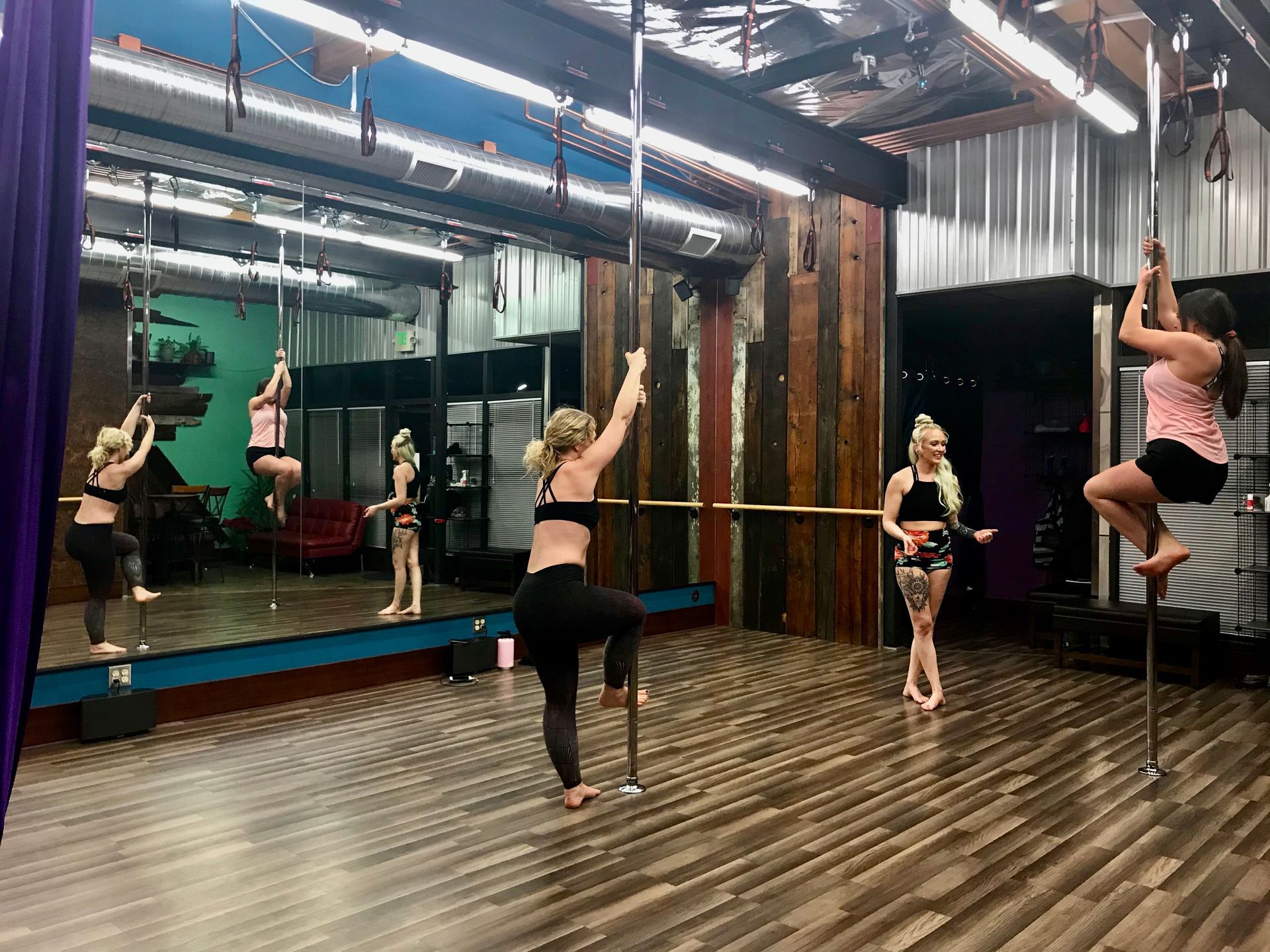 People practicing pole dancing in a mirrored studio with wood floors and ceiling lights