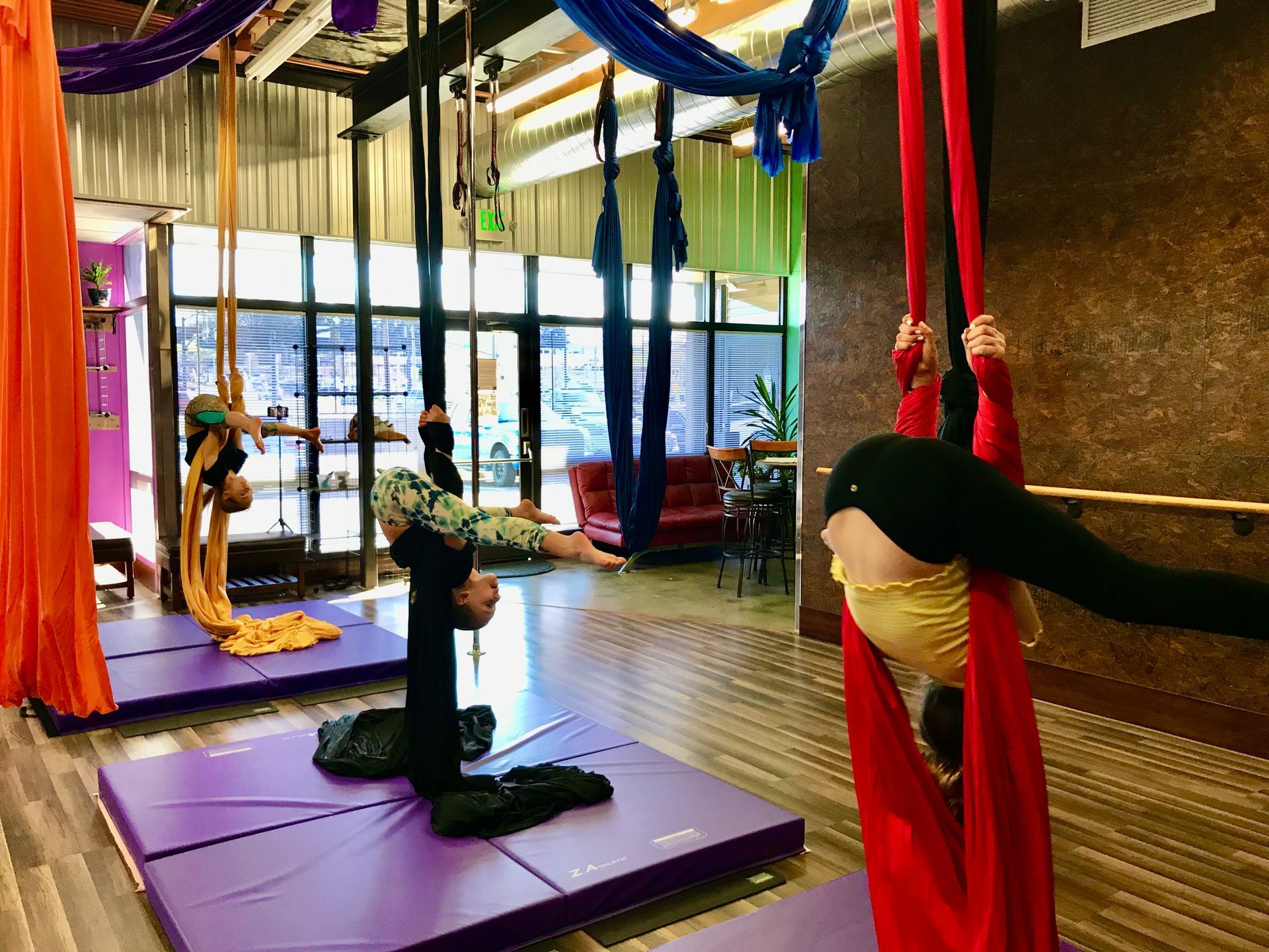 Two people practicing aerial silk yoga on red and purple hammocks in a studio