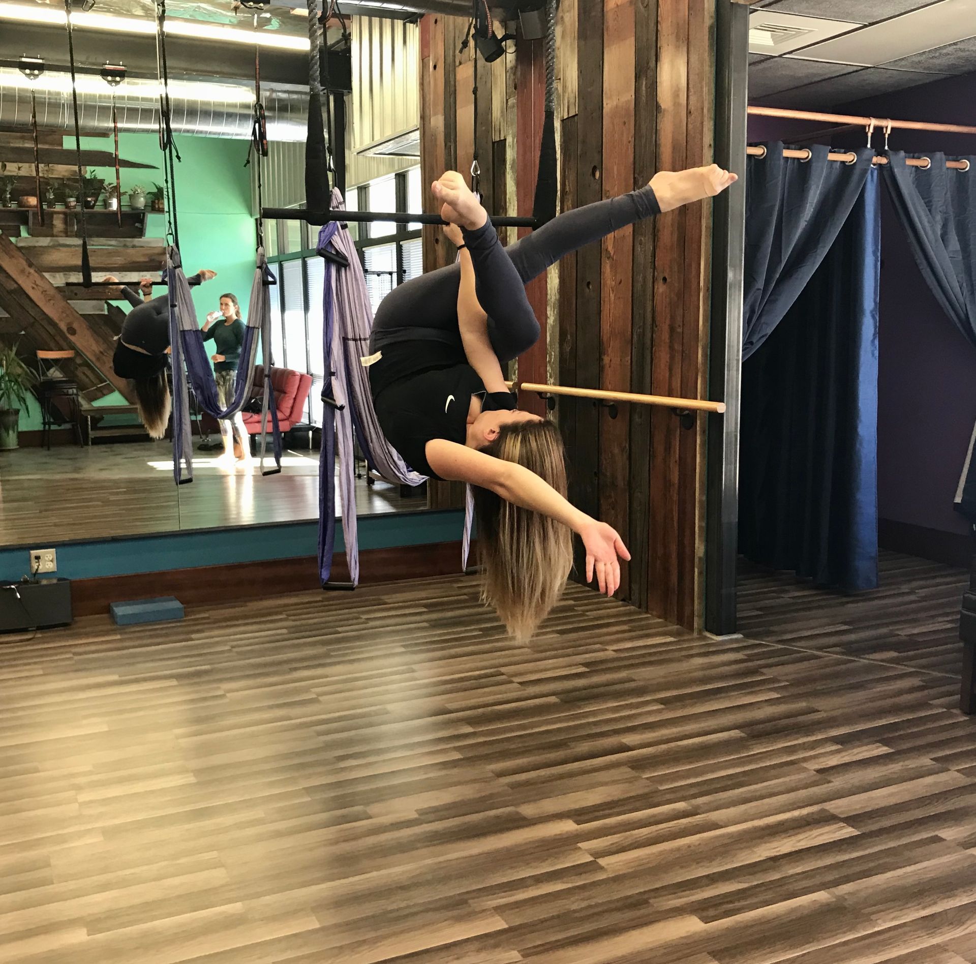 Person performing an aerial split pose in a dance studio with mirrors and curtains.
