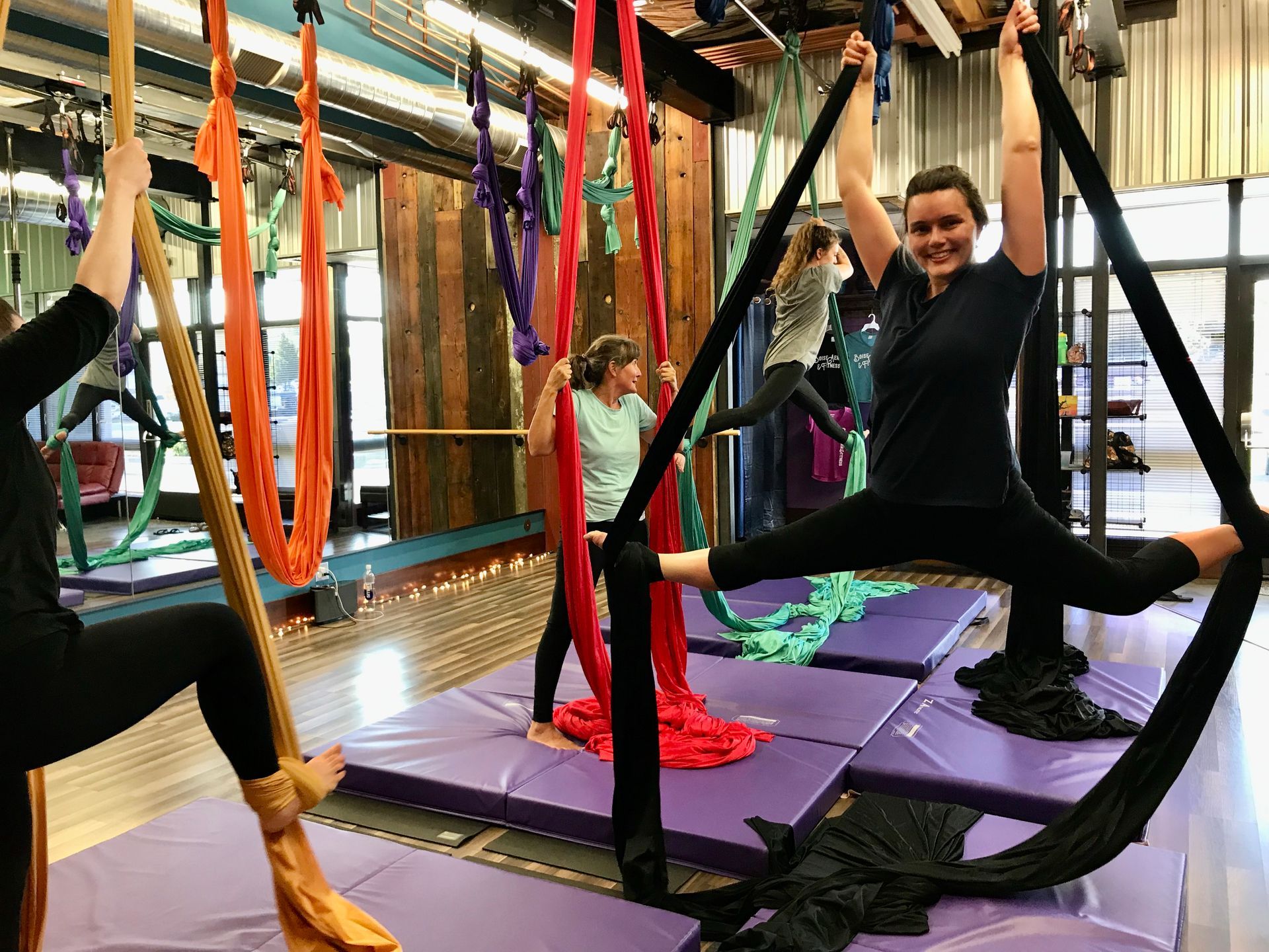 People doing aerial yoga in colorful hammocks at an indoor studio.