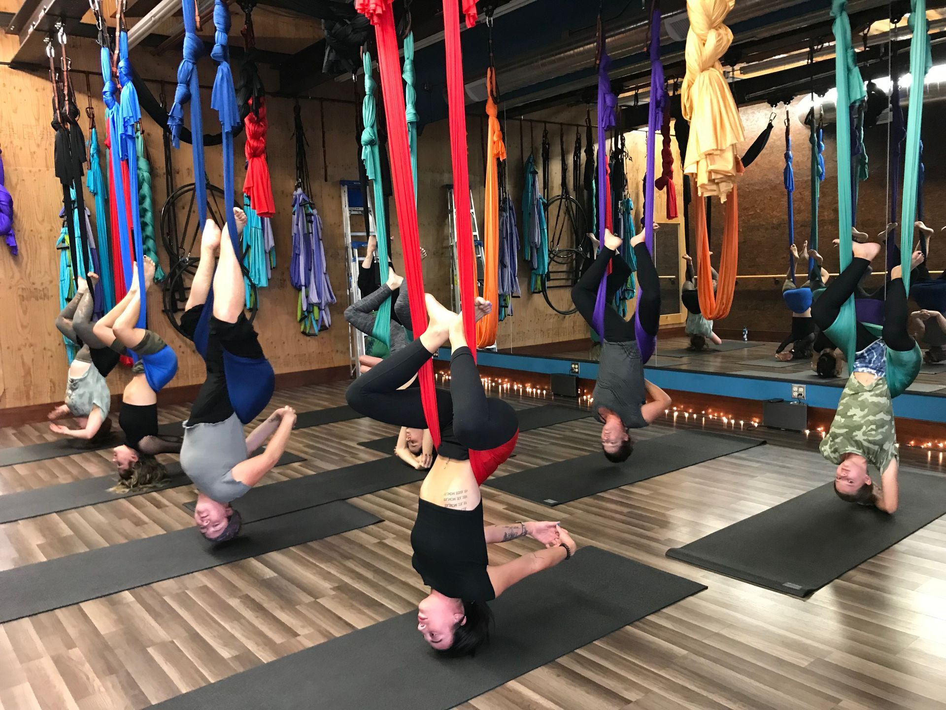 People practicing aerial yoga in a studio, inverted in colorful silk hammocks on mats.