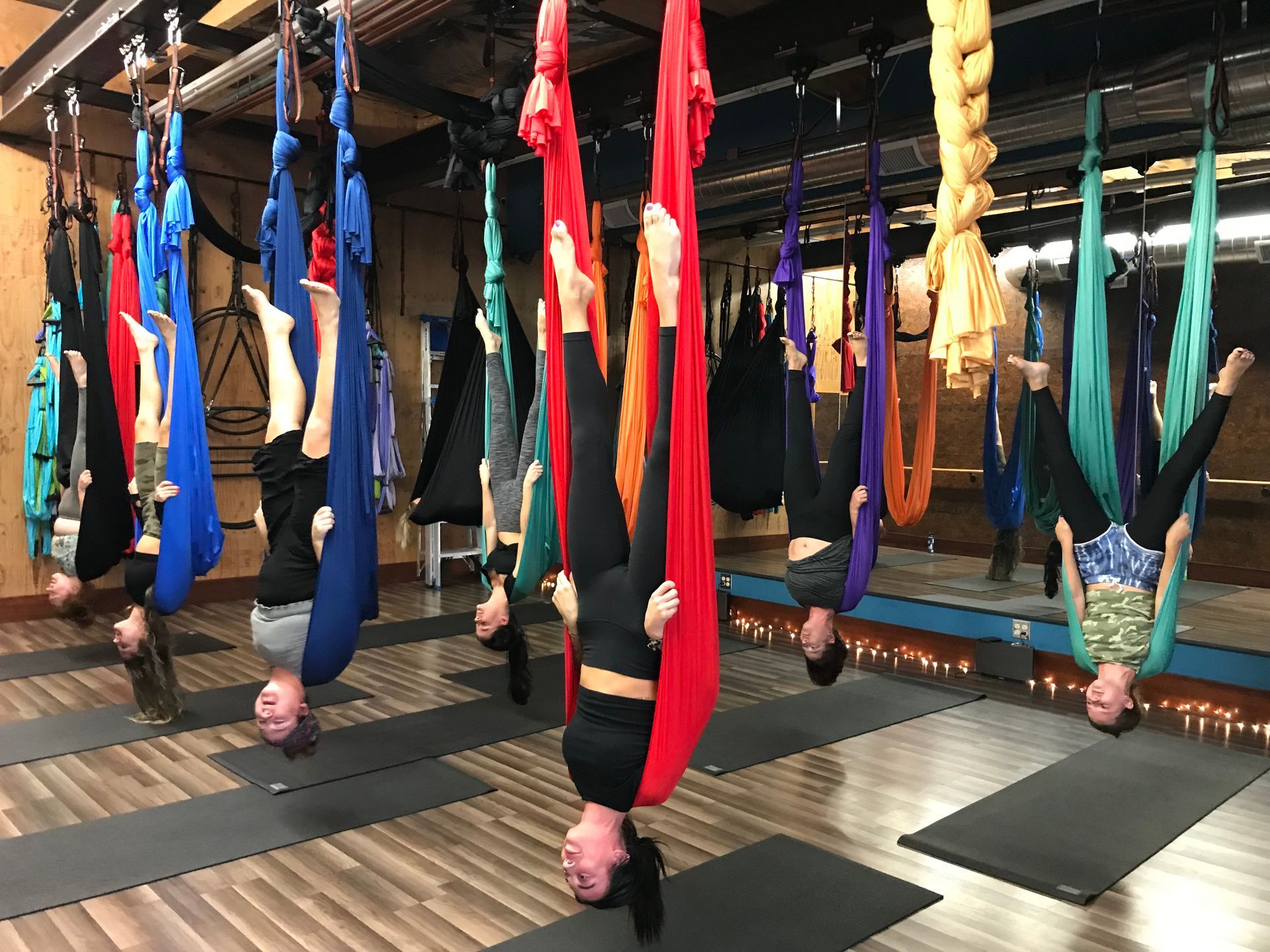 People hanging upside down in colorful fabric swings in a studio class