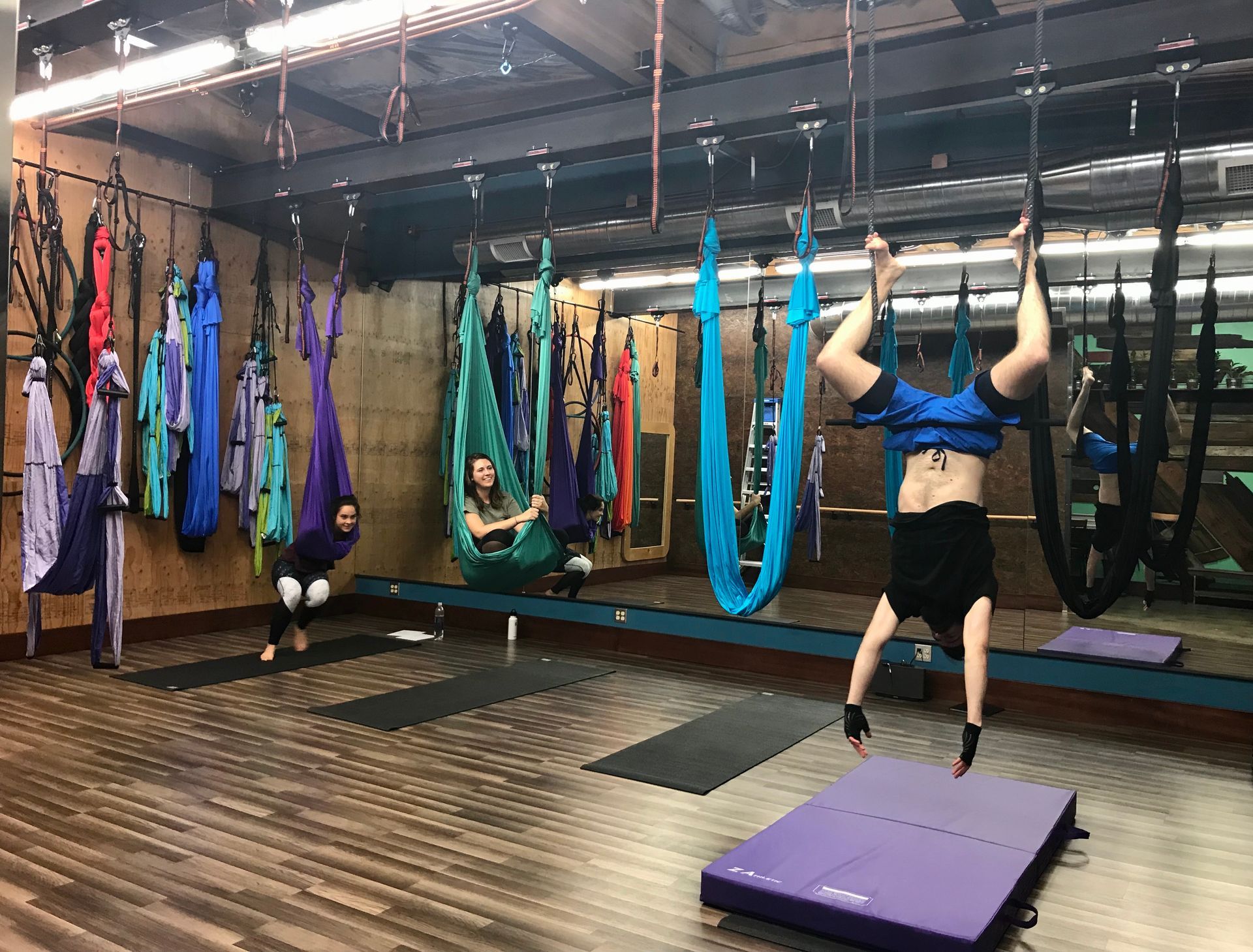 People doing aerial yoga in a studio with colorful hammocks and mats
