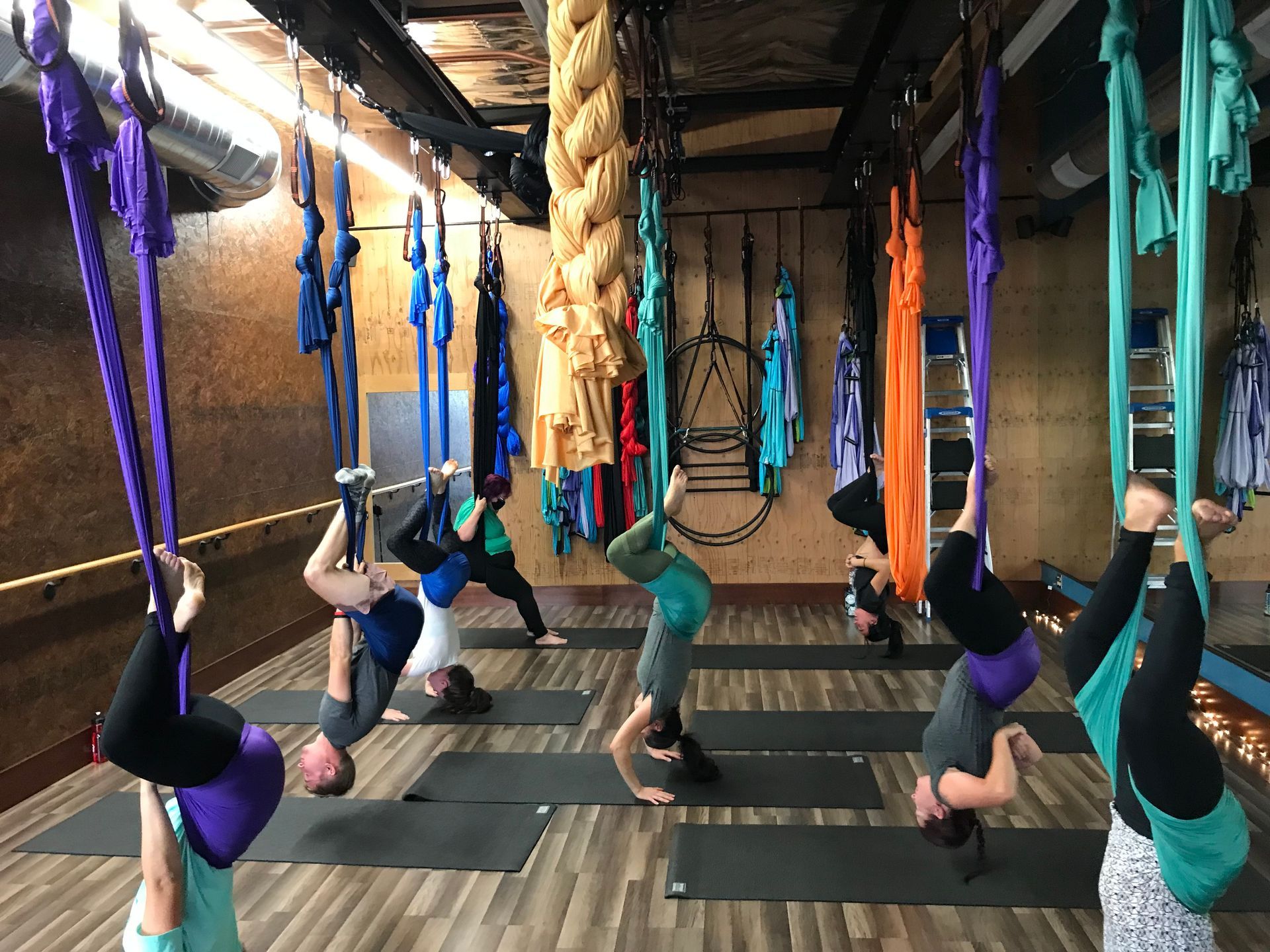 People practicing aerial yoga in hammocks in a studio with mats and exposed brick walls