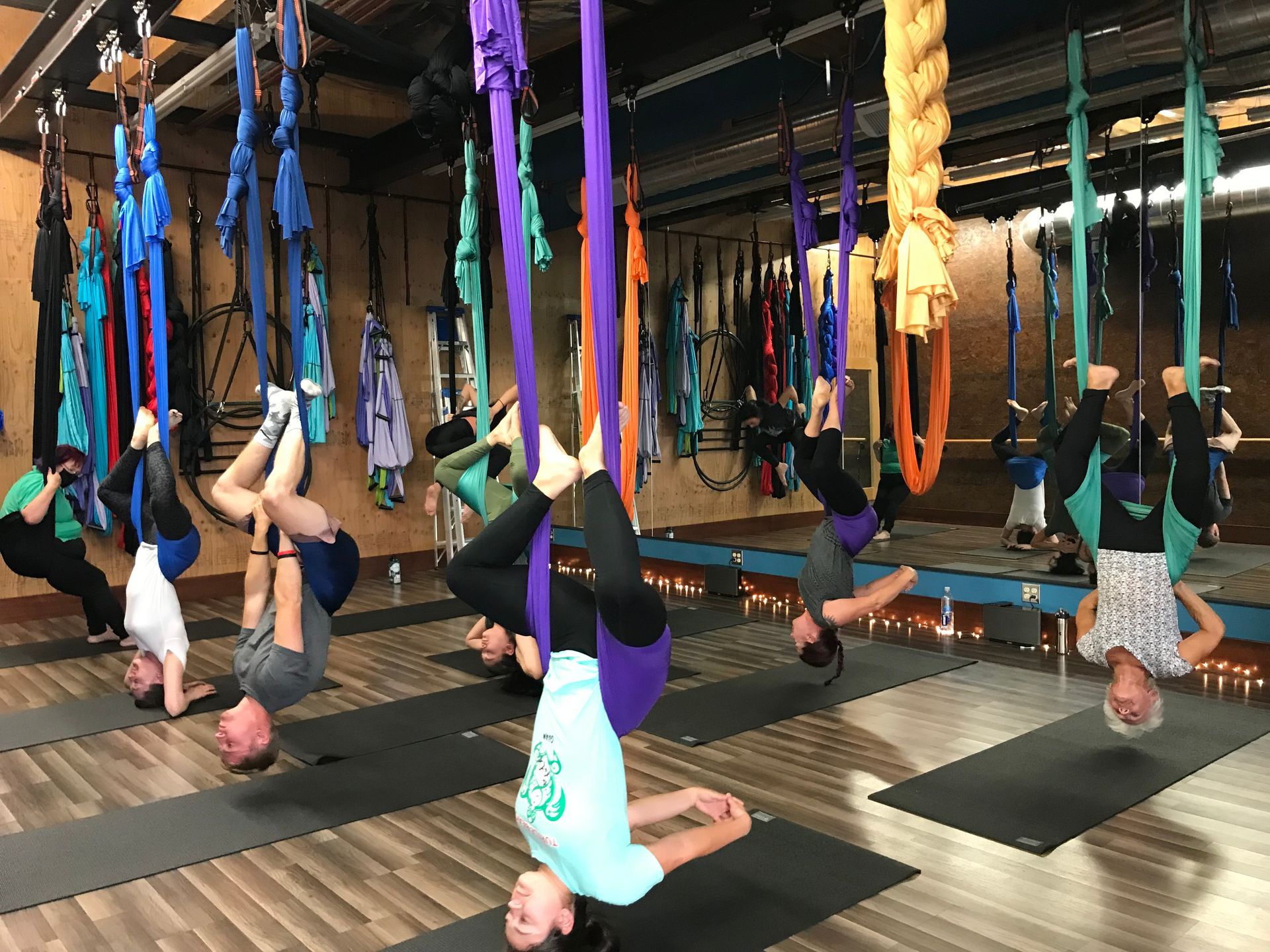 People doing aerial yoga inversions on hanging hammocks in a studio, with mats on the floor