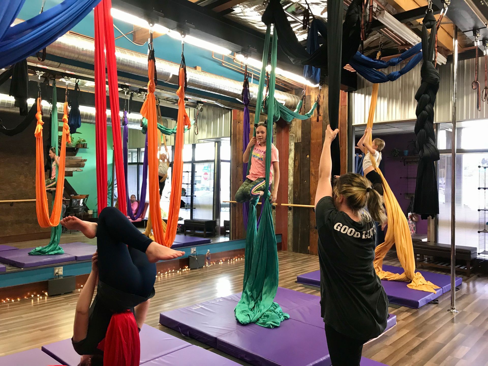 People doing aerial yoga on hanging hammocks in a studio with mirrors and colorful fabric hammocks