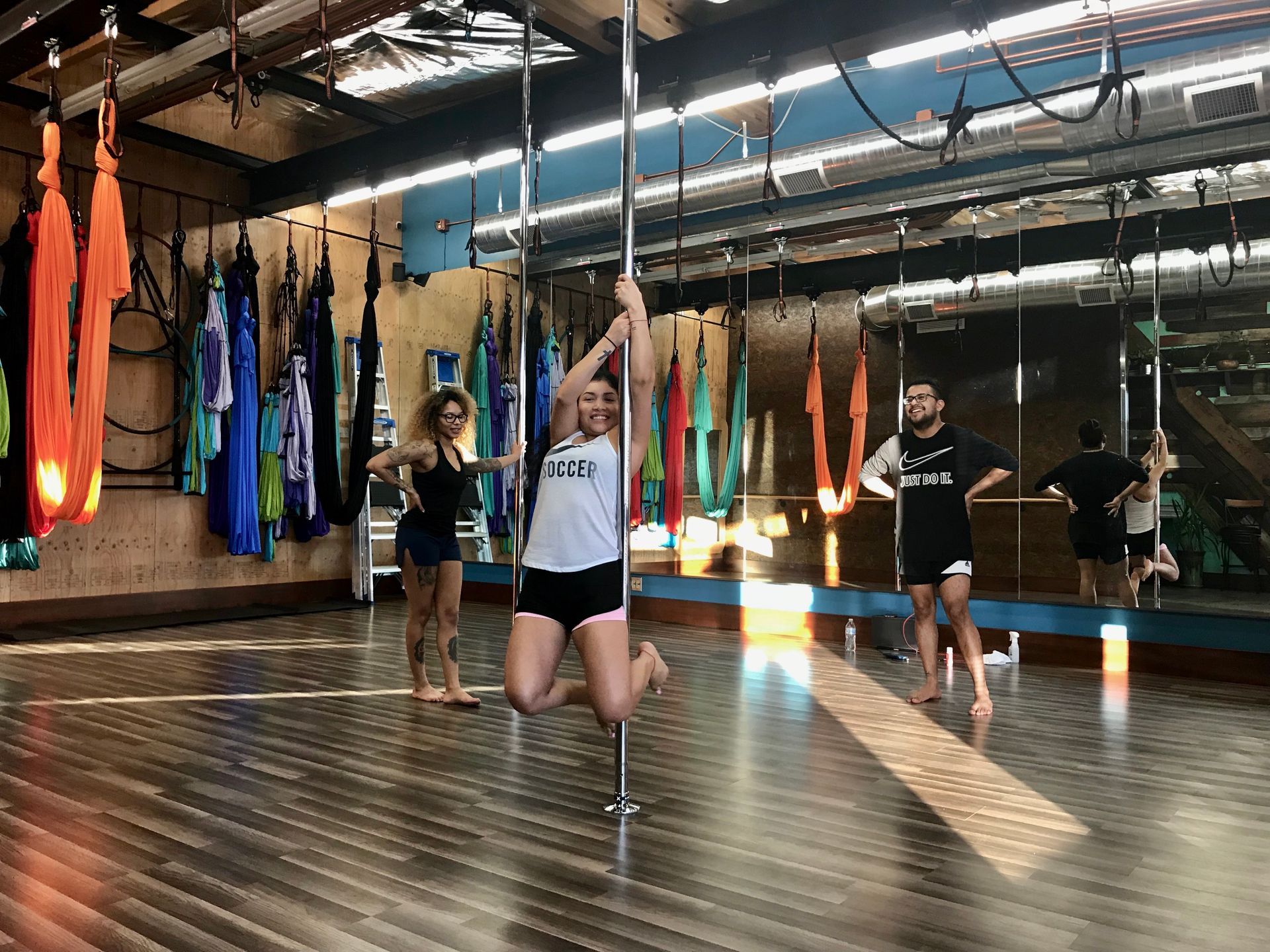 People practicing pole dance in a studio with mirrored walls and colorful aerial silks.