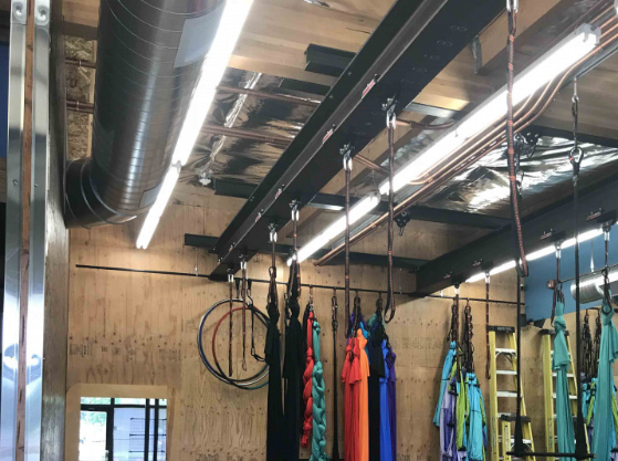 Indoor climbing gym ceiling with hanging ropes, fluorescent lights, and colorful climbing gear racks