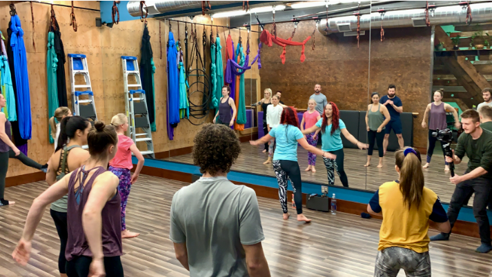 People doing a group fitness class in a studio with hanging aerial silks and a mirrored wall.