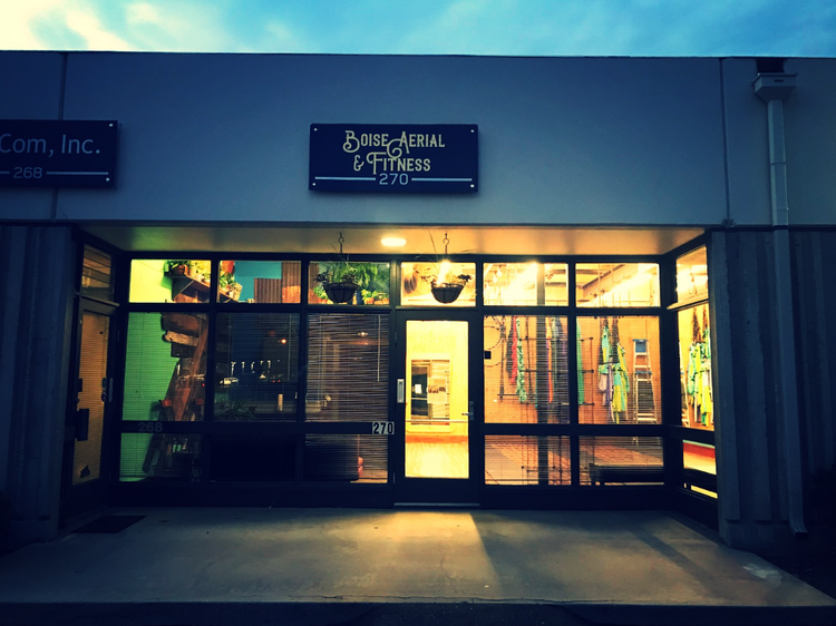 Storefront with lit windows at dusk, featuring a central glass door and illuminated sign above.