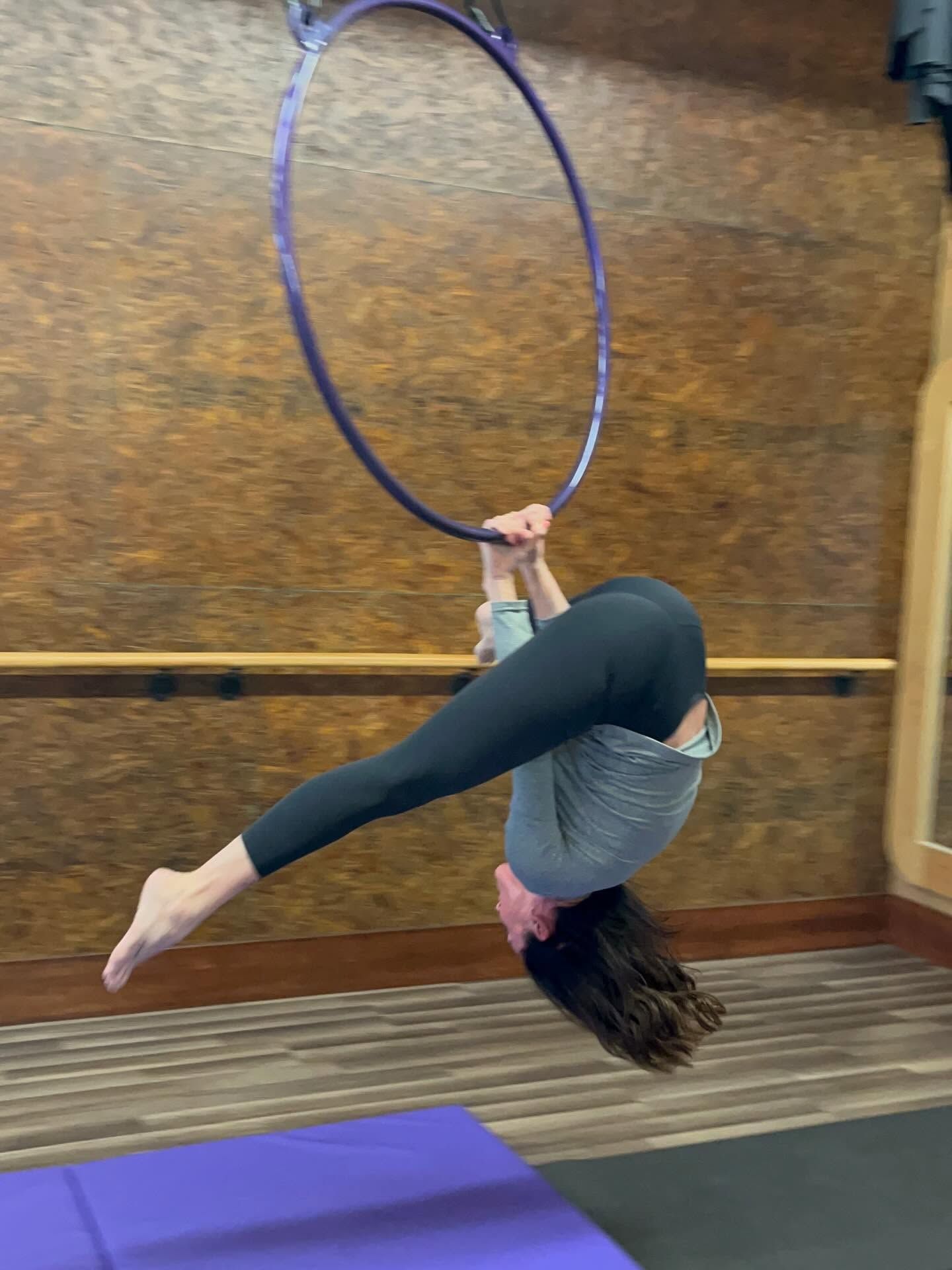 Person performing an aerial pose on a purple hoop in a studio setting